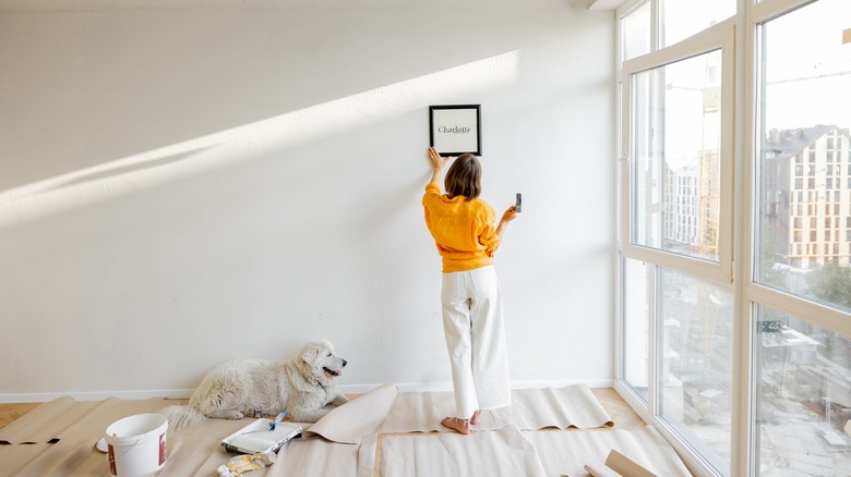 woman hanging picture painted wall