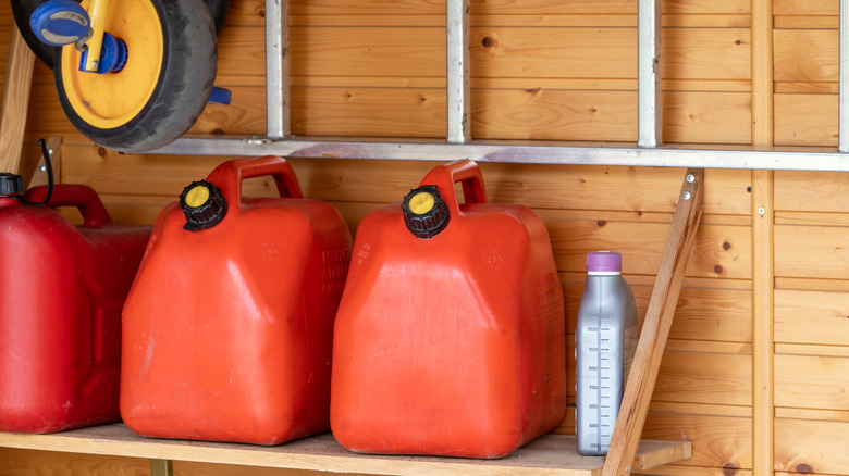 Three red gas containers sit on a shelf in a wooden shed