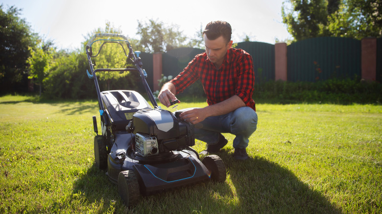Man checks his lawn mower's engine before mowing the lawn.