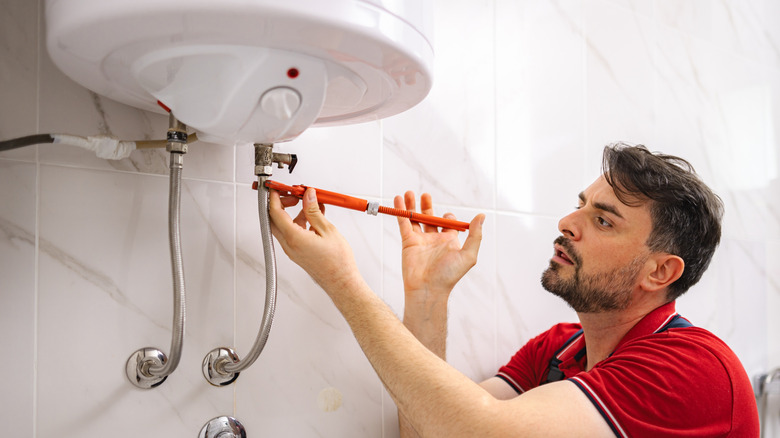 A man installing an electric water heater into a bathroom.