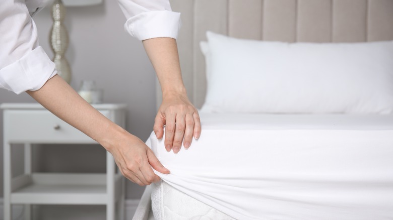 Person making bed with white sheets