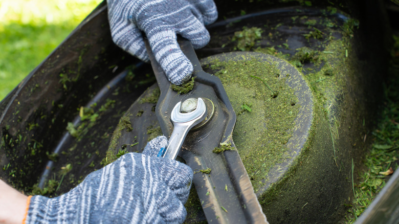 a person removes a nut from a lawn mower blade to prepare for sharpening it