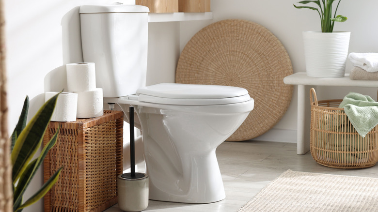 Toilet brush in container next to white toilet and wicker stand
