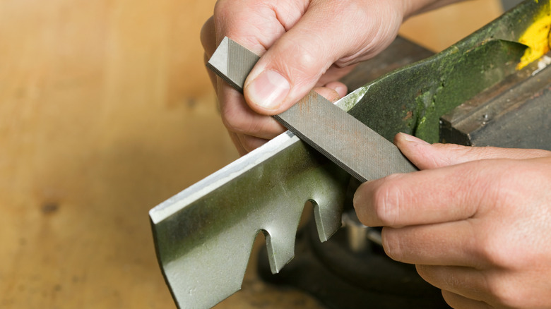 person sharpening and maintaining lawn mower blades