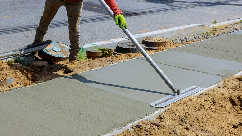 Worker smoothes concrete sidewalk