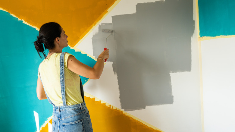 A woman painting a wall in different shades using a roller