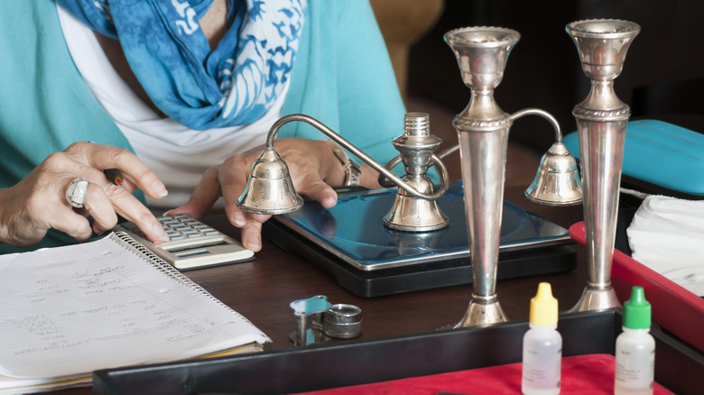 A person calculating the value of silver with a scale and calculator