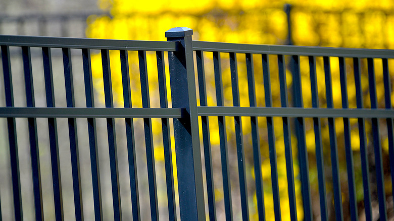 Closeup of a black aluminum fencepost, part of a fence with repeating vertical black metal bars