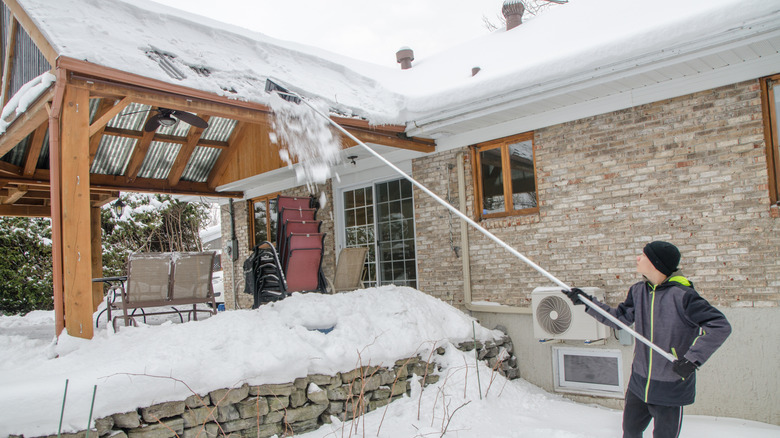 Person using a long roof rake to remove snow from a house roof