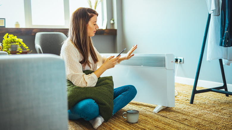 Girl sitting on the floor, using her phone to program a white smart space heater