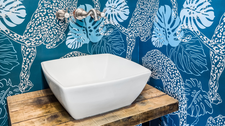 A white vessel sink in a powder room covered in a blue cheetah-print wallpaper.