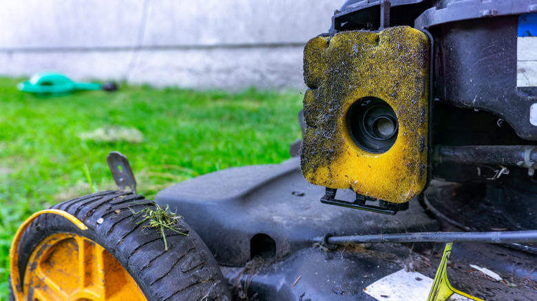 A dirty air filter clogged with dust and grass debris on the side of a lawn mower.