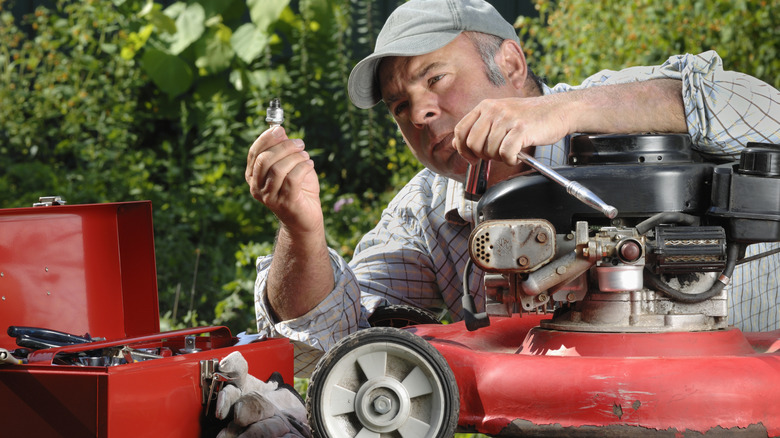 person working on lawn mower and holding up small mechanical piece