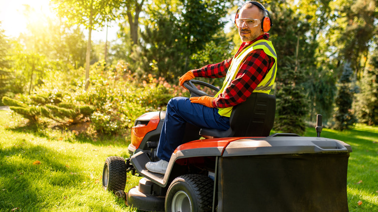 Man in safety gear using a riding mower in yard.