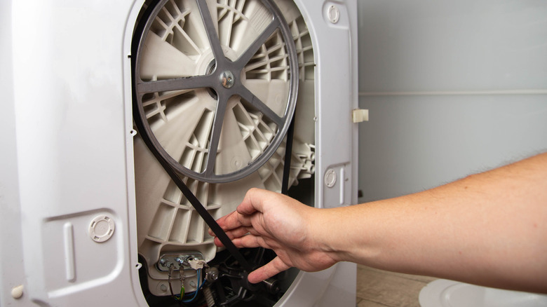 a person pulls on a washing machine belt to check the tension