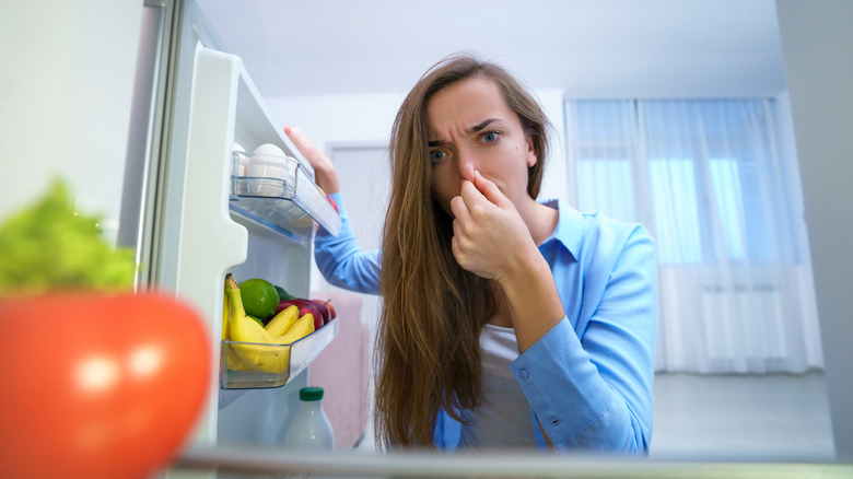 A woman looking into her fridge while plugging her nose