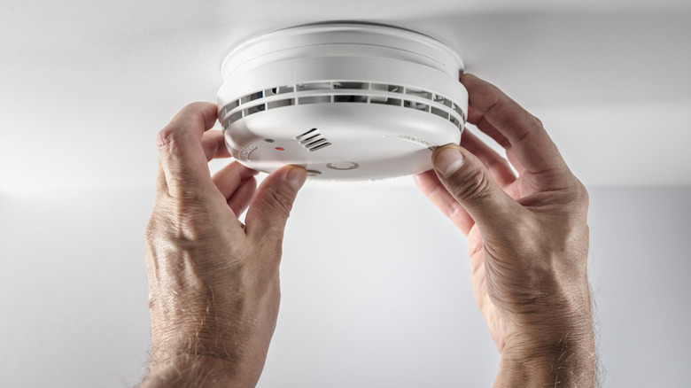 Two hands messing with a smoke detector on the ceiling