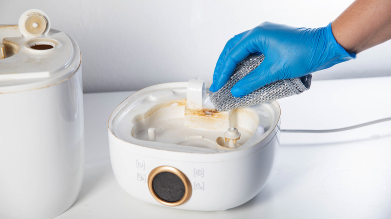 A glove hand wiping and cleaning scale and rust from a chemical agent in a humidifier.