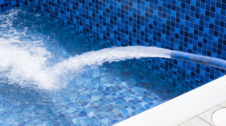 Water running from a hose and filling a pool with blue tiles