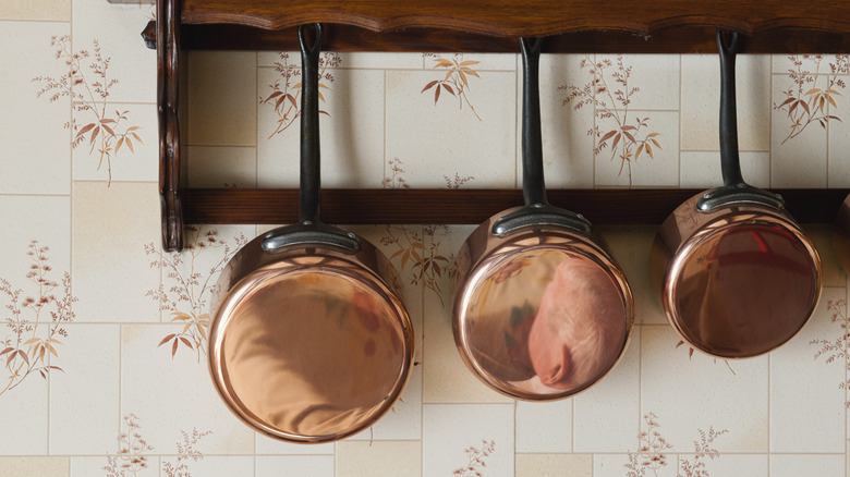 Three polished copper pots hang from a wooden rack