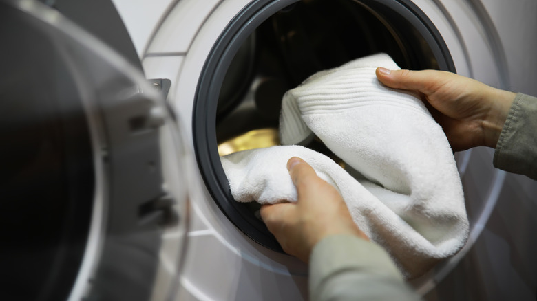 Hands putting white towel into washing machine