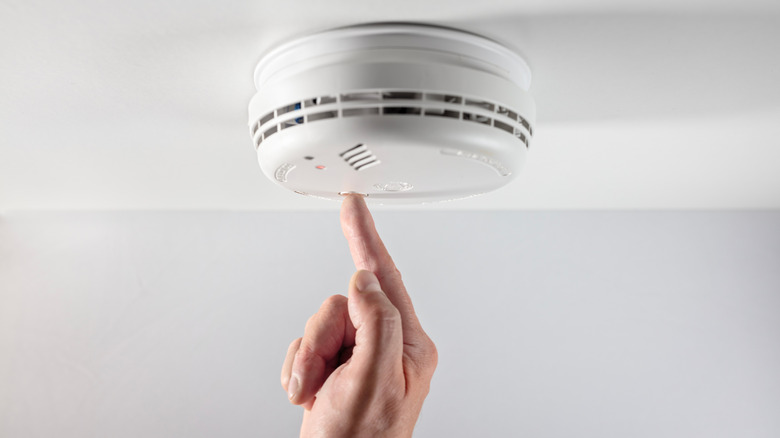 Finger pushing the test button on a smoke detector