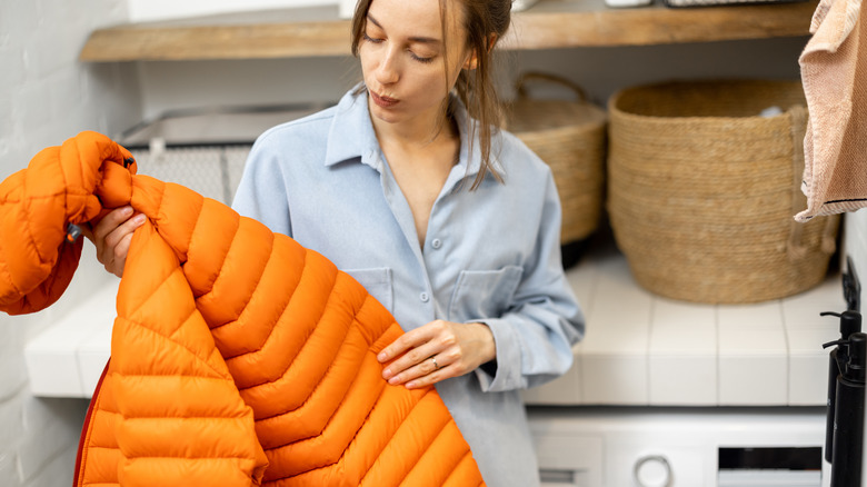 Woman standing in front of a washing machine, holding an orange jacket