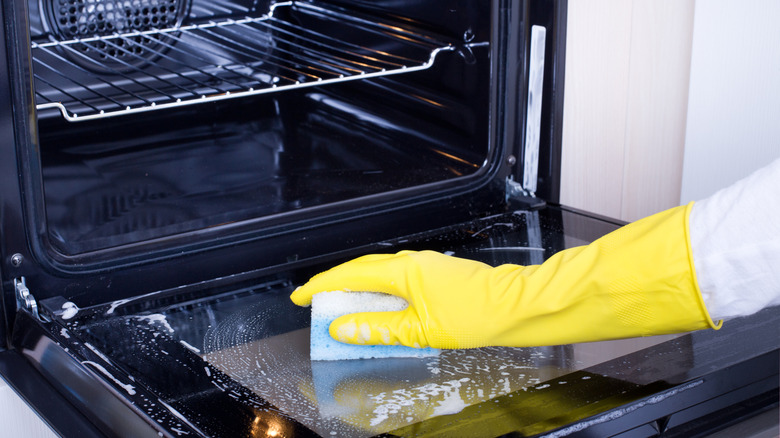 A hand cleaning an oven glass door.
