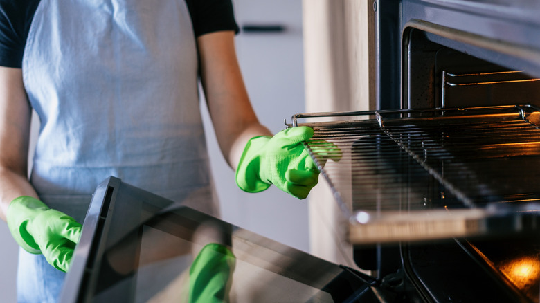 A woman wearing gloves and an apron cleaning her oven.