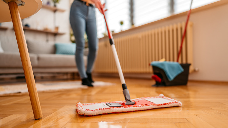 person drying hardwood floor with mop in background
