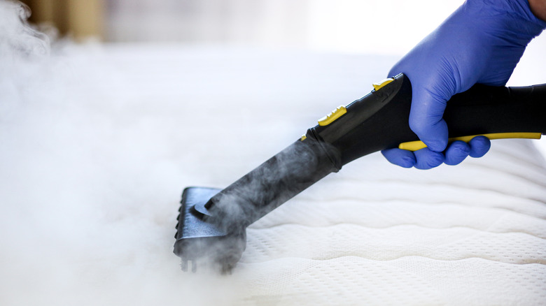 Person steam cleaning the surface of a mattress