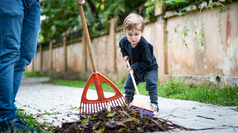 Father and son sweeping branches off sidewalk with broom and rake