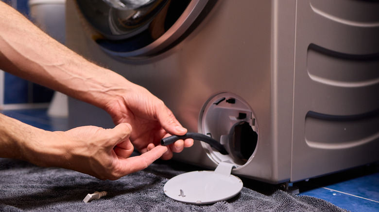 Close-up of a man's hands holding a washing machine drain pipe over a towel