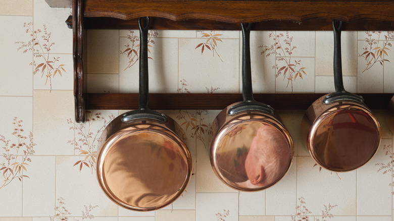 Three polished copper pots hang from a wooden rack