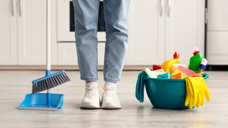 Close up of person standing next to broom and cleaning supplies