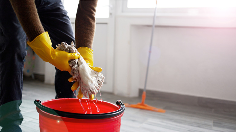 Close up of person wringing out mop head over a bucket