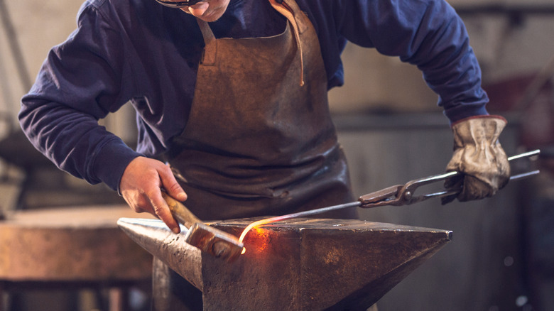 Man bending hot metal at an iron anvil.