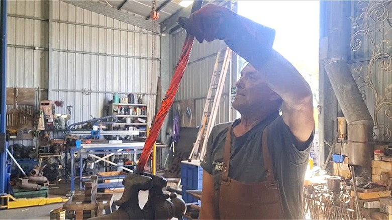 Metalworker and artist Adrian Beacham twisting red hot metal in his workshop.