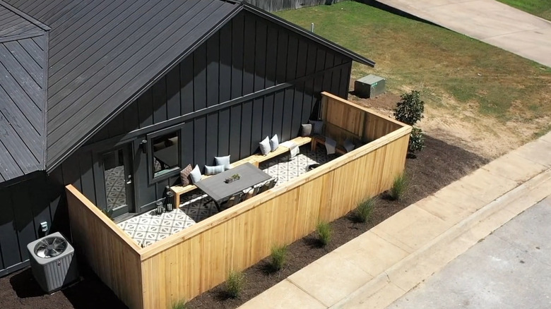 Exterior of black house with light wooden fence around patio