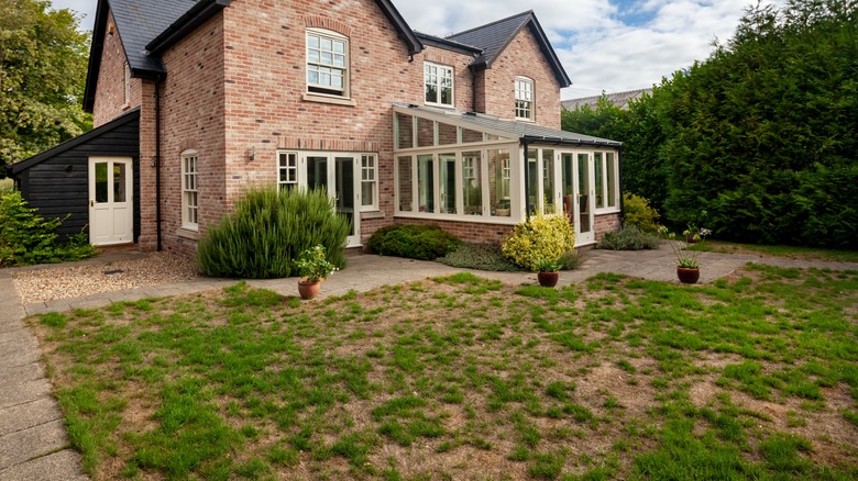 brick house with patchy grass lawn