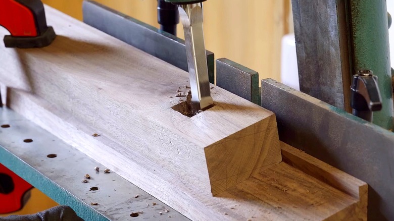 A mortising machine with a drill bit carving out a mortise in a piece of wood