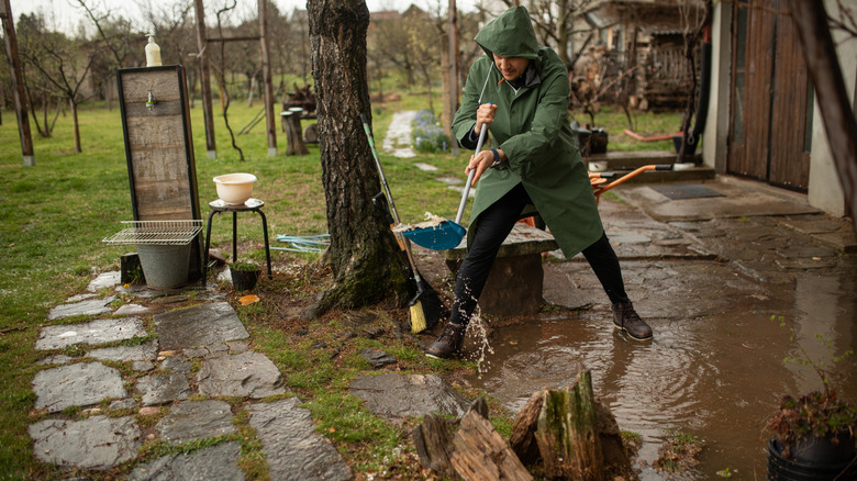A person wearing a green raincoat working in the yard to clear some stormwater that's pooling near the house