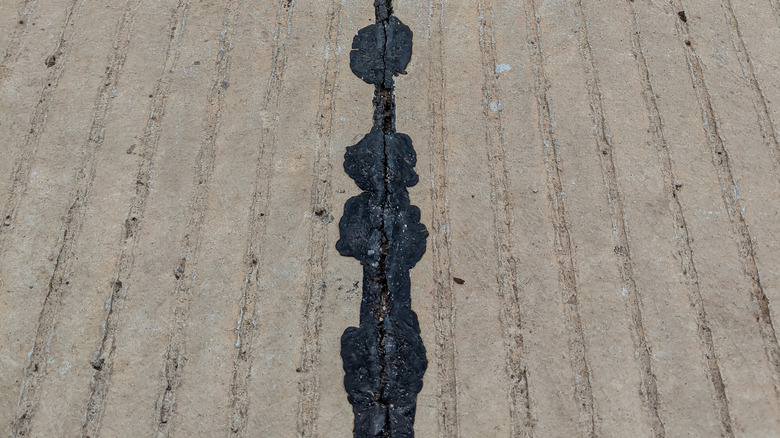 A stretch of concrete has a crack that is visibly filled with a line of black asphalt.