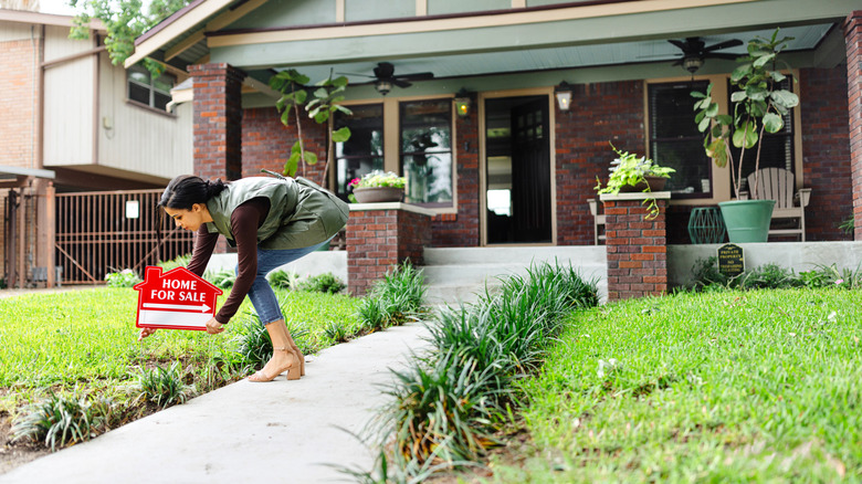 Woman putting for sale sign outside her house