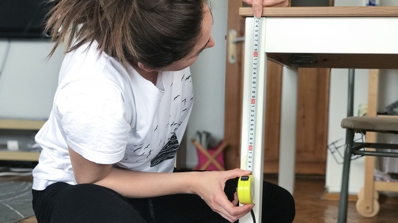 A woman measuring the height of a table