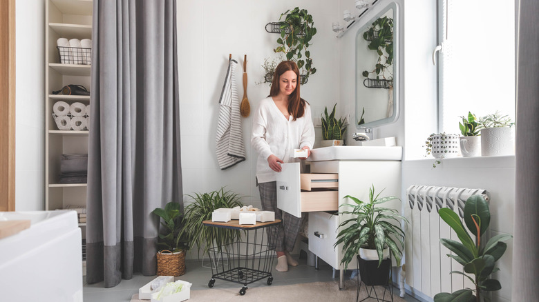 woman standing in front of open drawer of bathroom vanity organizing toiletries in drawer