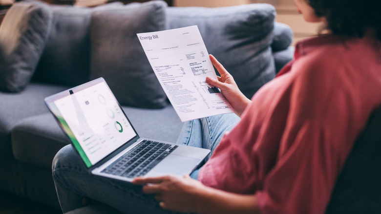 Woman holding a laptop in one hand and an electricity bill in another