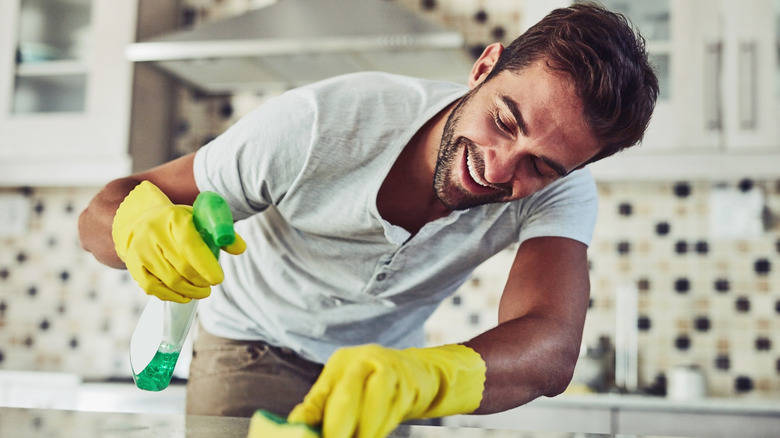 A smiling person spraying cleaner on a kitchen countertop