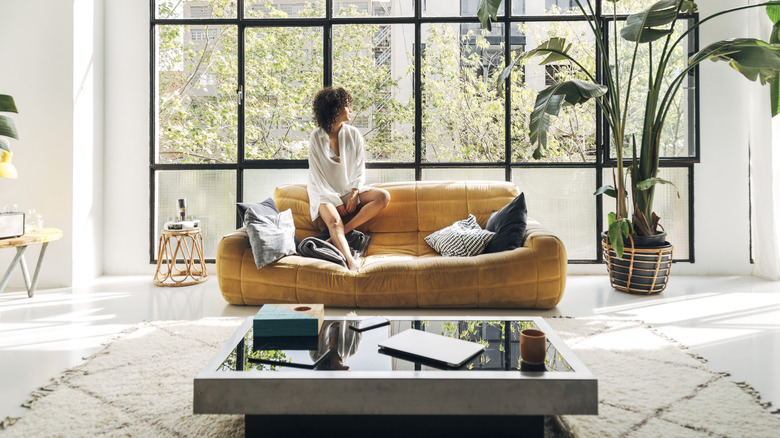 Serene young woman enjoying her bright and airy apartment living room, relaxing on a comfortable sofa amidst modern decor and lush plants