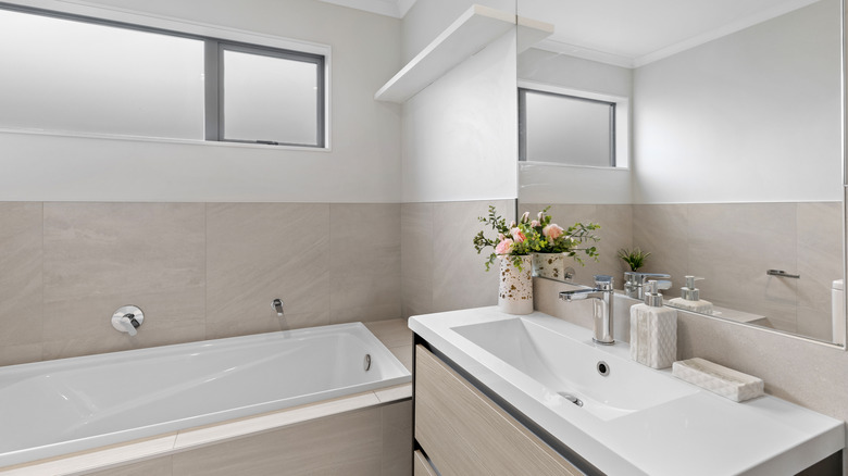Bathroom with white and off-white walls, tub, vanity, and clerestory window.